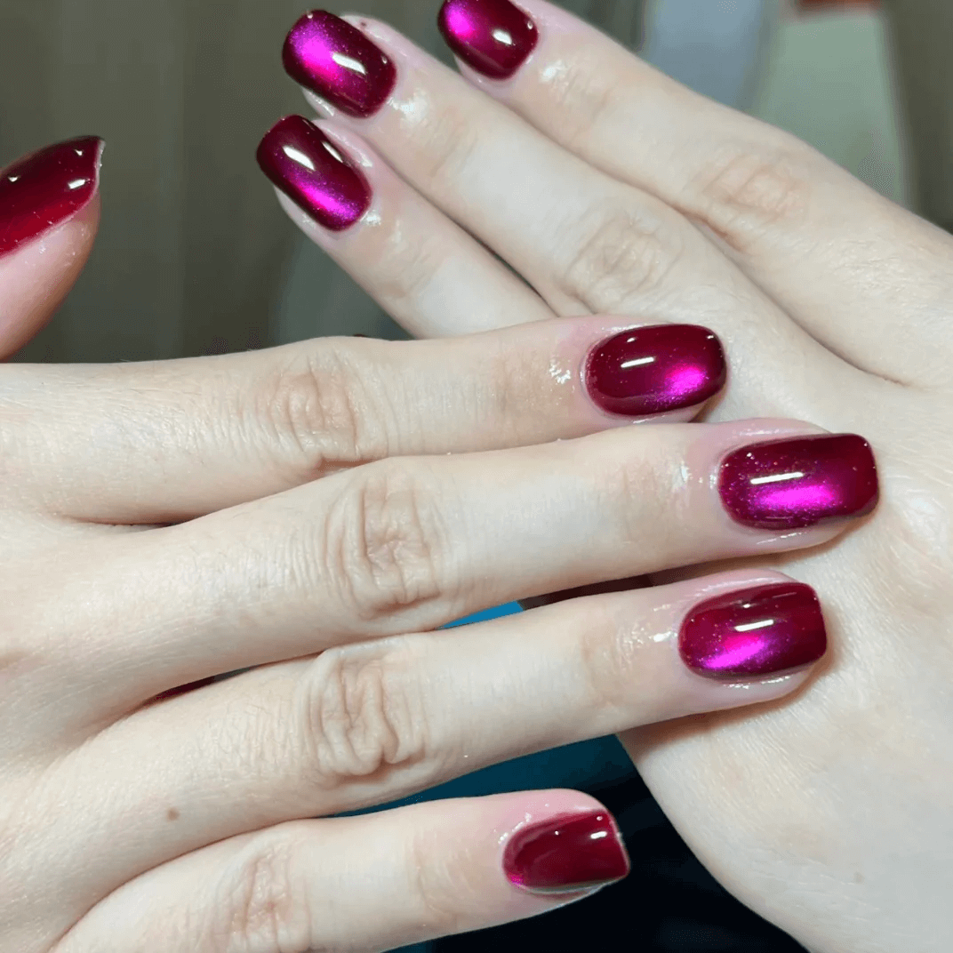 Shiny red magnetic cat eye gel polish producing a vibrant 3D nail effect with sparkling shimmer and reflective particles, creating a bright cat eye line across the nail for a striking professional gel manicure and glossy reflective nail design.