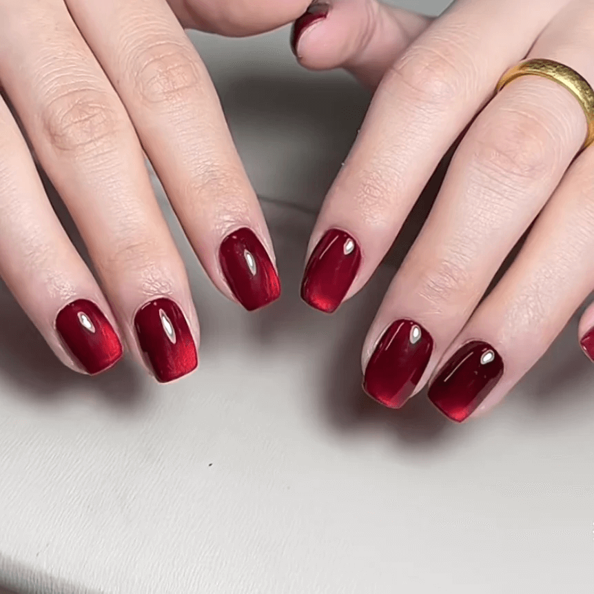 Dark red magnetic cat eye gel polish creating a deep luxurious 3D nail effect with rich shimmer and reflective particles, forming a bold glowing cat eye line across the nail for an elegant professional gel manicure and dramatic reflective nail design.