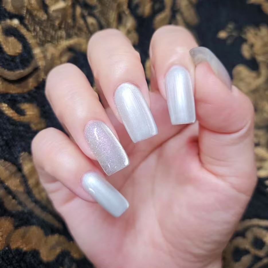 Snow white magnetic cat eye gel polish creating a luminous 3D nail effect with soft silver shimmer and reflective particles, forming a glowing cat eye line across the nail for an elegant professional gel manicure and clean reflective nail design.