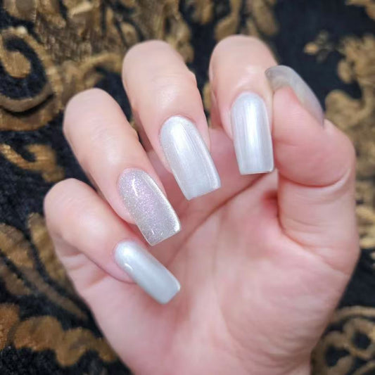 Snow white magnetic cat eye gel polish creating a luminous 3D nail effect with soft silver shimmer and reflective particles, forming a glowing cat eye line across the nail for an elegant professional gel manicure and clean reflective nail design.